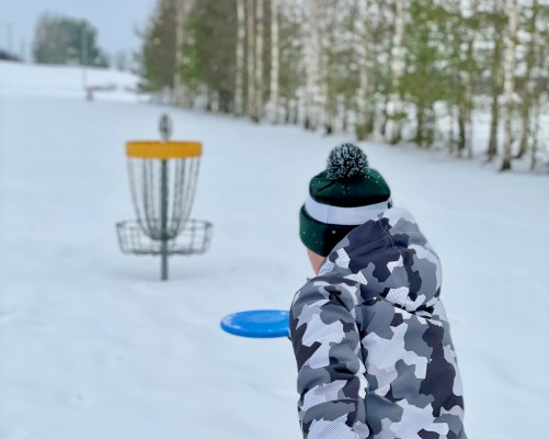 Lapsi heittää frisbeen koriin. On talvi.