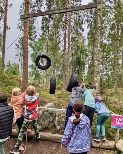 Barn håller i rep med hängande bildäck. De är i skogen.