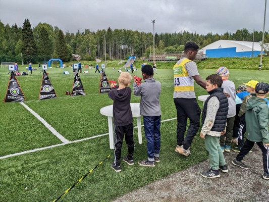 Elever står bredvid en gräsplan och skjuter på måltavlor.