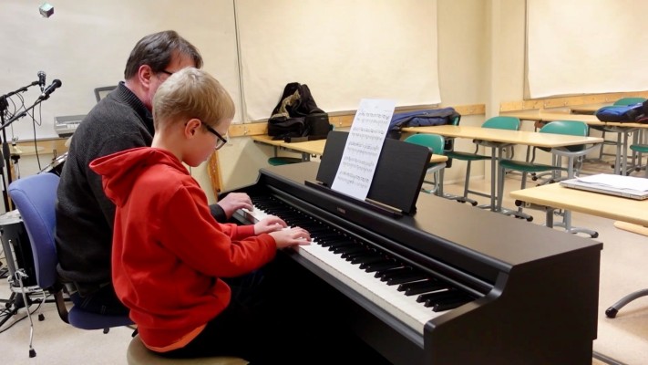 En pianoelev sitter vid pianot med sin musiklärare.