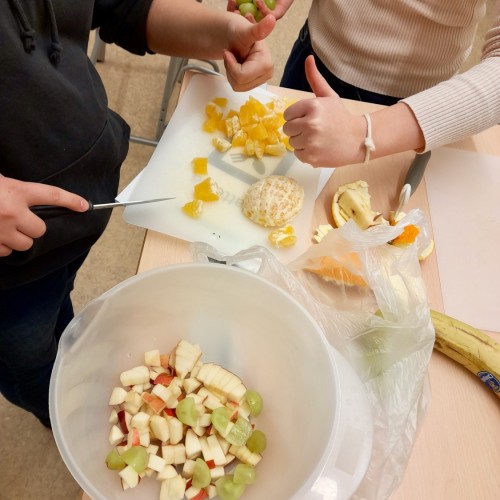 Hedelmäsalaatin valmistus. Kaksi oppilasta leikkaa hedelmiä pieniksi paloiksi ja laittaa ne muovikulhoon.