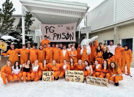 En stor mängd ungdomar klädda i orangea halare står utanför skolan. De har skyltar med texten PG-prison, help us med mera.