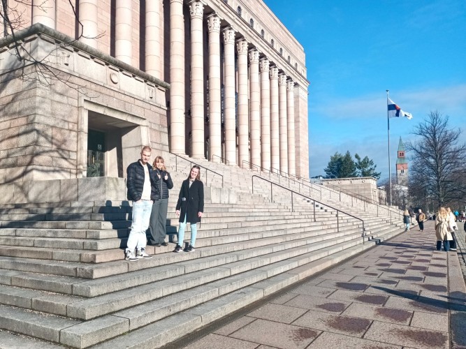 Tre ungdomar står på riksdagshusets trappa i Helsingfors.
