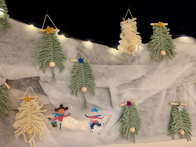 Julpynt i form av ett vinterlandskap med granar av garn och två figurer som skrinnar på is.