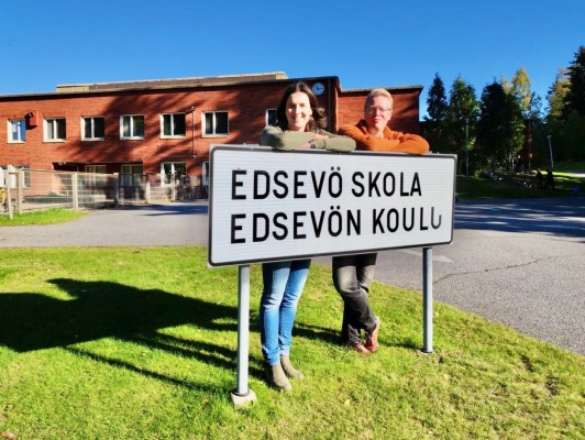 Rehtorit Hanna ja Mika seisovat kyltin takana. Kyltissä lukee Edsevö skola / Edsevön koulu.