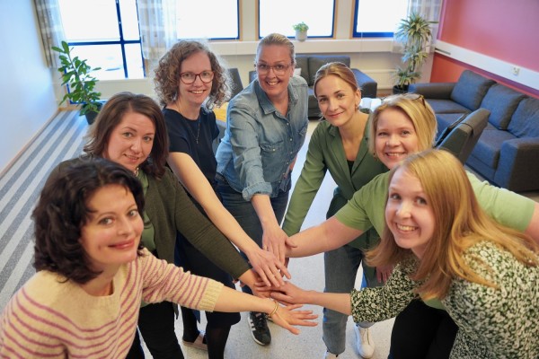 Oppilashuollon piirissä töitä tekevät seitsemän naista seisoo ympyrässä ja pitelee toisiaan kädestä. Ne katsovat suoraan kameraan.