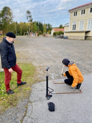 En lärare står på skolgården och ser på när en elev förbereder raketuppskjutning. I bakgrunden syns Bennäs skola.