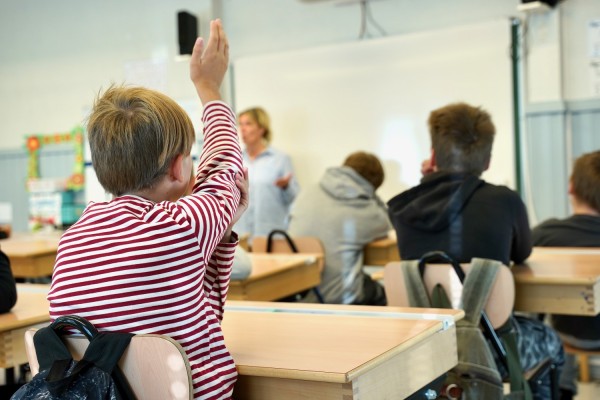 Oppilas pitää kättään ilmassa kun hän istuu luokkahuoneessa.
