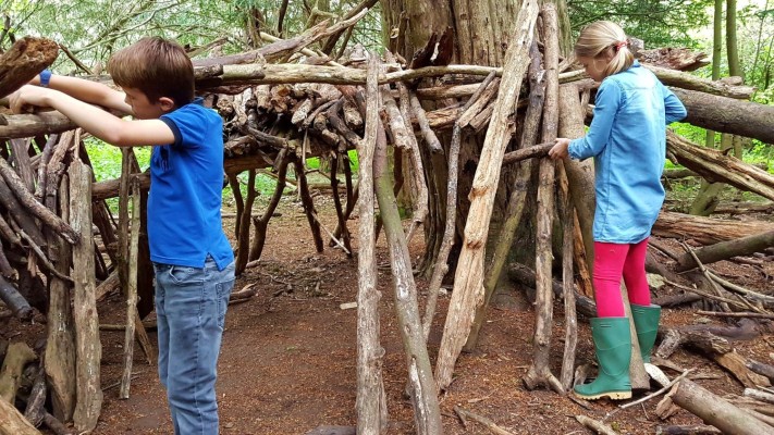 En pojke och en flicka bygger en koja av trädgrenar.