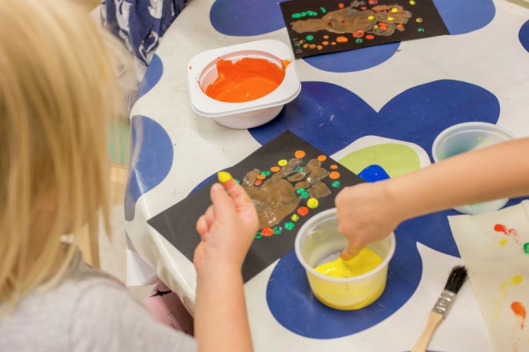 Barnhänder målar med olika färger på ett papper.