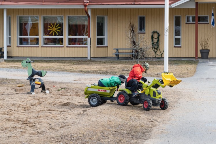 Två barn leker med en tramptraktor på en daghemsgård.