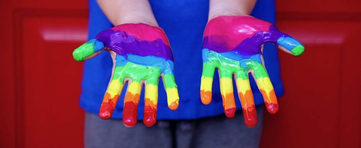 Ett par barnhänder målade i regnbågens färger.