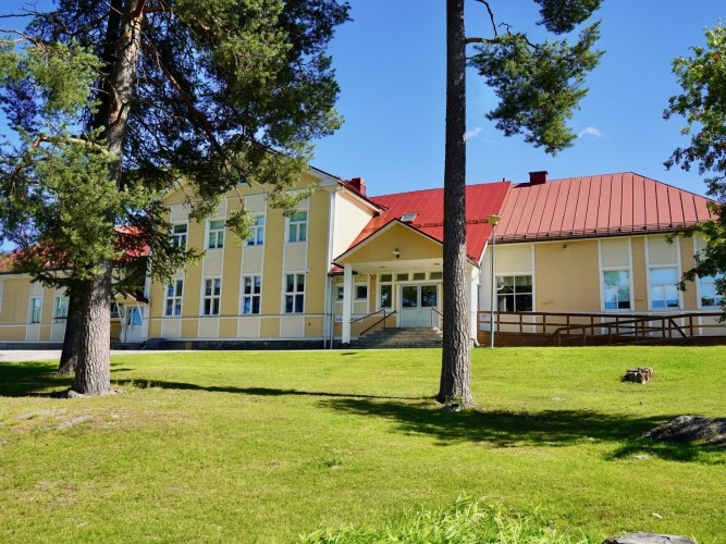 Kållby skolas fasad med gräsplan framför. Solen skiner.