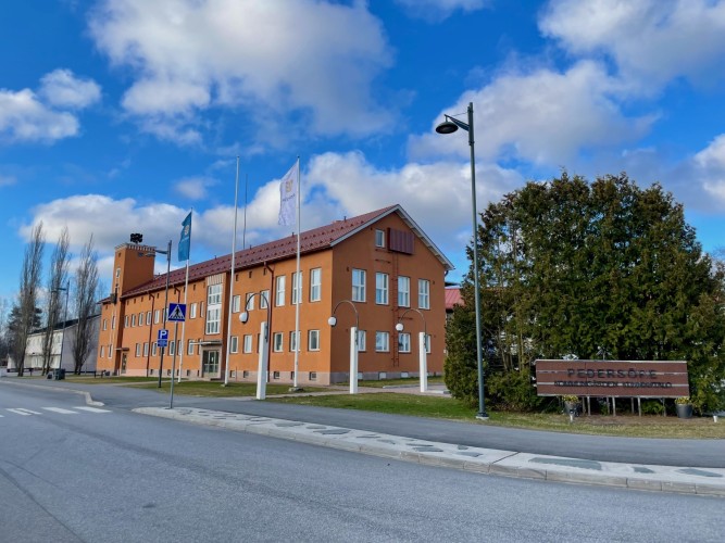 Pedersöre kommungård fotograferad från gatan. Tre flaggor hissade, Finlands flagga och kommunens flagga.