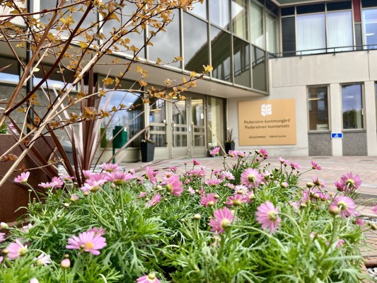 Blommor i förgrunden, och kommungården och en stor infoskylt i bakgrunden.