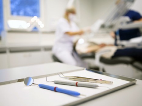 En bild från en tandläkarmottagning. På bordet finns verktyg som tandläkare använder. I bakgrunden syns personer i arbetskläder.
