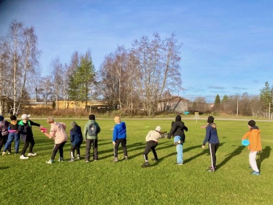 Elever står på rad och kastar frisbee mot en korg.