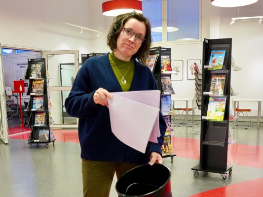 Ulrika Stenmarkilla on paperipino toisessa kädessään ja heittää paperit toisessa kädessään pitelemäänsä roskakoriin.