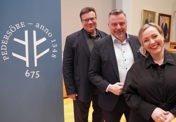 Juhlavuoden logoplakaatti ja sen vieressä seisovat kunnanvaltuuston puheenjohtaja Niclas Sjöskog, kunnanjohtaja Stefan Svenfors ja kunnanhallituksen puheenjohtaja Johanna Holmäng.