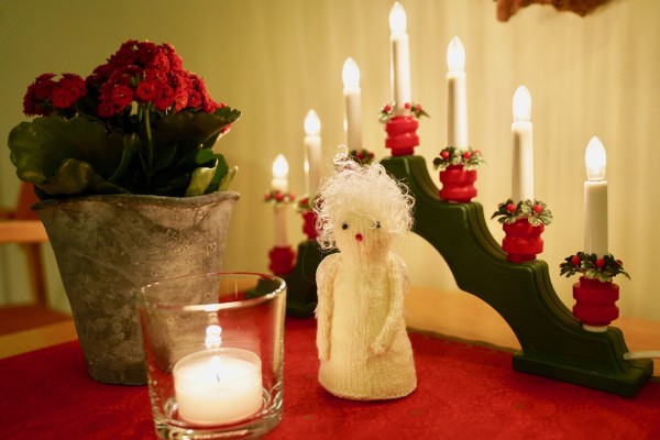 Sähkökynttilänjalka, pieni palava kynttilä ja enkeli pöydällä.